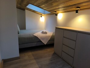Ein gemütliches Schlafzimmer mit Oberlicht, einem Bett mit gerolltem Handtuch und einer kleinen Küchenzeile.