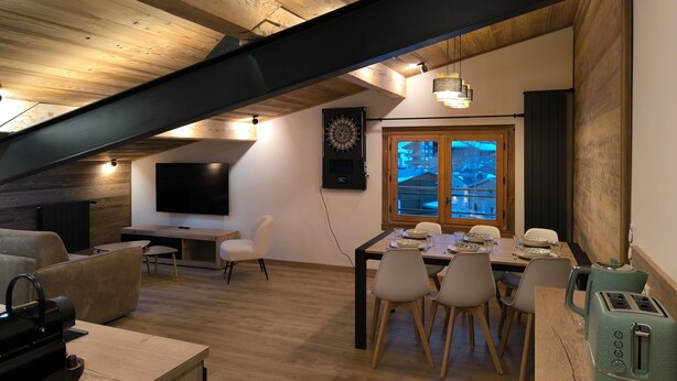 Ein gemütlicher Loftraum mit Essbereich, Holzbalkendecke, großem Fenster und Flachbildfernseher.