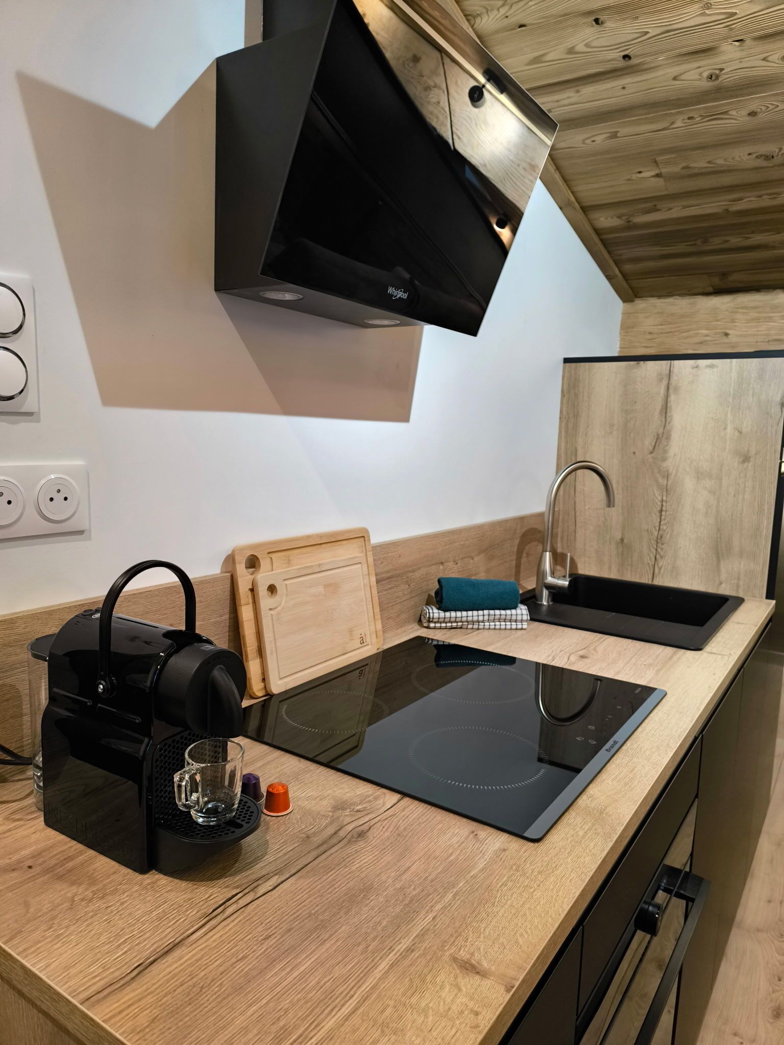 Eine moderne Küche mit einem schwarzen Induktionskochfeld, einer Holz Arbeitsplatte, einer schwarzen Dunstabzugshaube, einer integrierten Spüle und einem Holzschnittbrett.