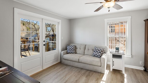 A room with a beige sofa, patterned pillows, a ceiling fan, a window with a view, and a wooden floor. - Red Door Cottage | 1/2 Mile to Whiskey Row (Prescott)