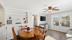 A dining area with a wooden table and chairs, a ceiling fan, a television, and a view through the sliding glass doors. - Red Door Cottage | 1/2 Mile to Whiskey Row (Prescott)