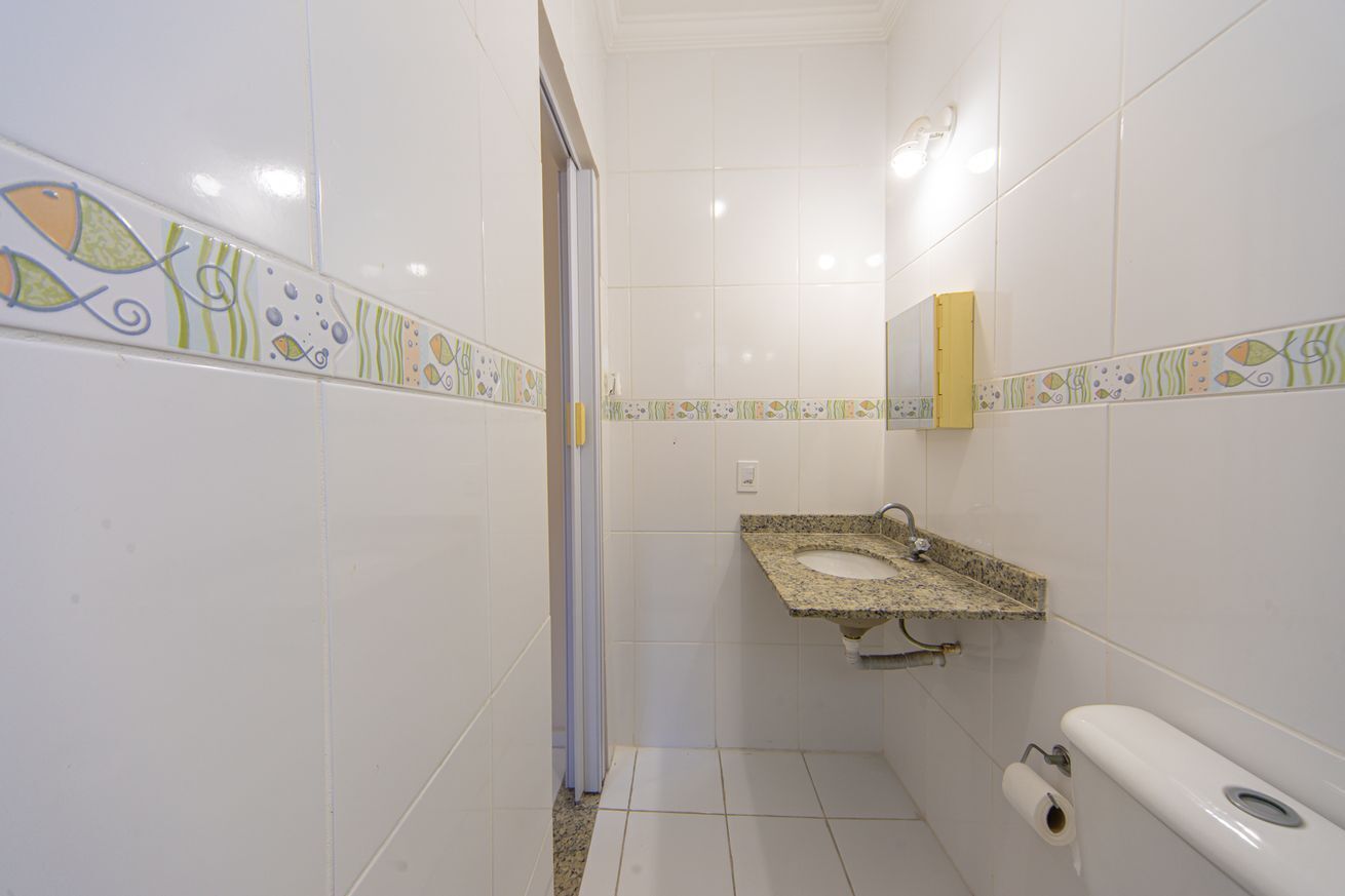 A bathroom with white tiled walls, a granite sink, a toilet, and a shower area.