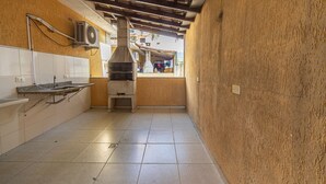 A narrow kitchen with a built-in oven, white tiled walls, and a wooden ceiling. - Sua Casa na Enseada Perto da Praia e de Tudo (Guarujá)