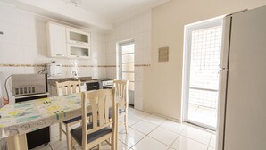 A kitchen with white cabinets, a microwave, a stove, and a dining table with chairs. - Sua Casa na Enseada Perto da Praia e de Tudo (Guarujá)