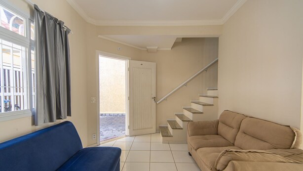 A living room with a blue sofa, beige sofa, and a staircase leading to a door. - Sua Casa na Enseada Perto da Praia e de Tudo (Guarujá)