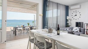 A room with a dining table, chairs, a sofa, a clock, and a view of the sea. - Beachfront Villa Victoris – Private Sunbeds (Podstrana)