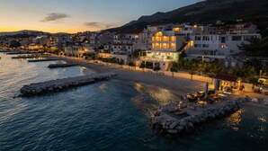 A coastal town at dusk with buildings, a beach, and a pier. - Beachfront Villa Victoris – Private Sunbeds (Podstrana)
