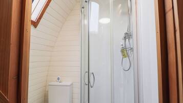A small, enclosed shower area with a glass door, a toilet, and a wooden ceiling.