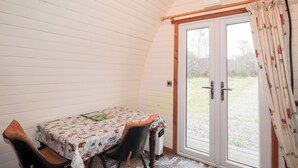 Un pequeño comedor con una mesa cubierta por un mantel, dos sillas y una puerta que da al exterior.