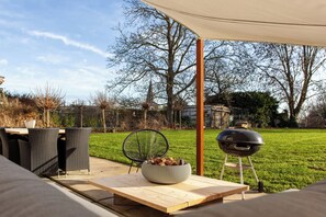 An outdoor patio area with a wooden table, wicker chairs, a grill, and a covered seating area.