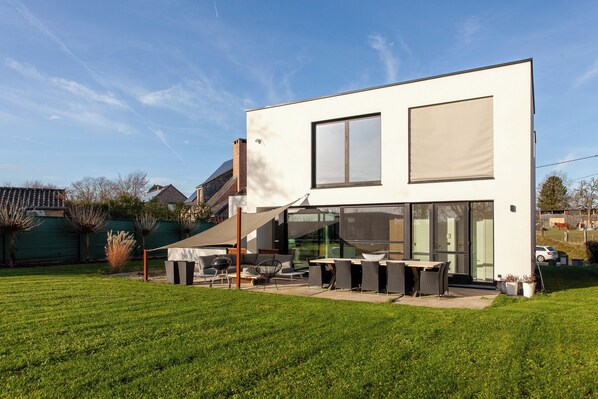 A modern two-story house with a patio area featuring outdoor furniture and a barbecue grill.