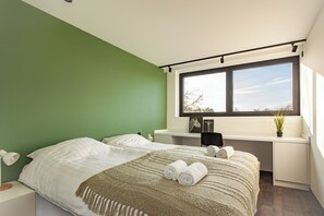 A bedroom with a bed, a desk, a window, and a green wall.