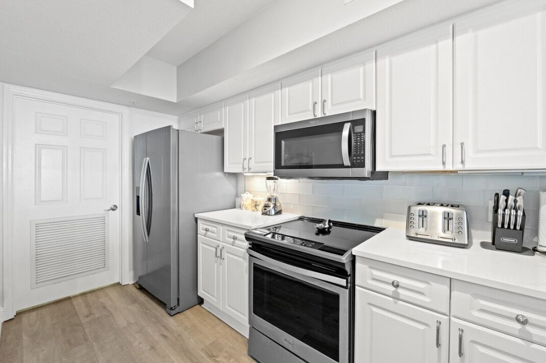 A modern kitchen with white cabinets, a stainless steel refrigerator, a microwave, a stove, and a toaster.