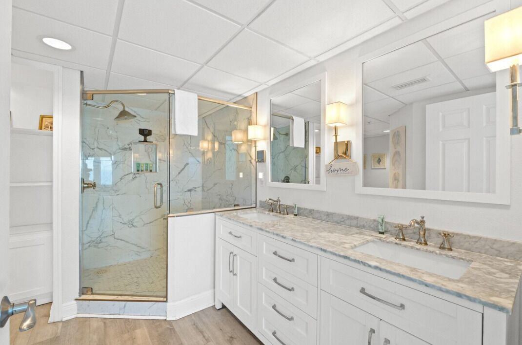 A modern bathroom with a glass-enclosed shower, marble countertops, and a large mirror.