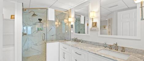 Un baño moderno con ducha de vidrio, encimeras de mármol y un espejo grande.
