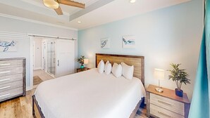 Ein Schlafzimmer mit einem großen Bett, einem Deckenventilator, einem Nachttisch mit Lampe und einer Zimmerpflanze.