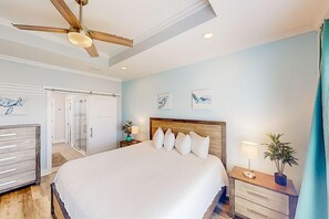 A bedroom with a large bed, a ceiling fan, a nightstand with a lamp, and a potted plant. - Turtle Beach Retreat (Panama City Beach)