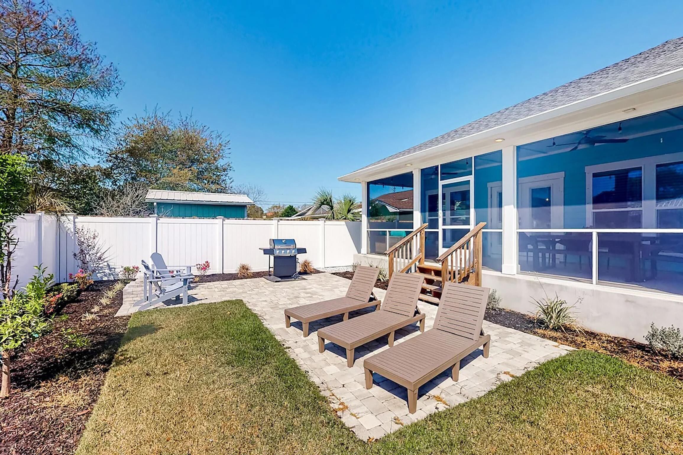 Un jardin avec un barbecue, des chaises longues et un patio couvert.