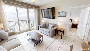 Ein Wohnzimmer mit einer Couch, einem Couchtisch, einem an der Wand montierten Fernseher und einem Balkon mit Meerblick.