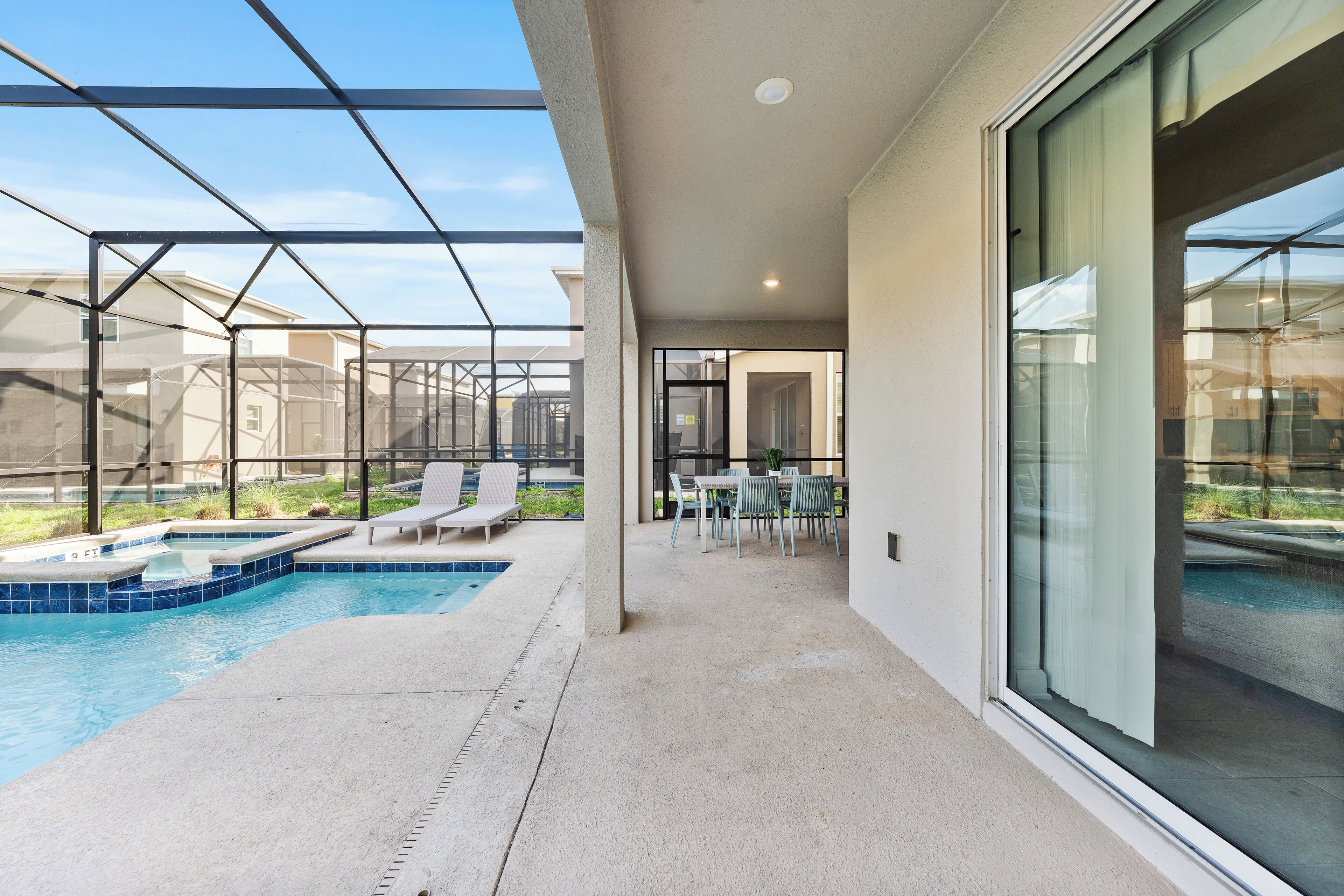 A modern outdoor pool area with glass walls, lounge chairs, and a dining table.