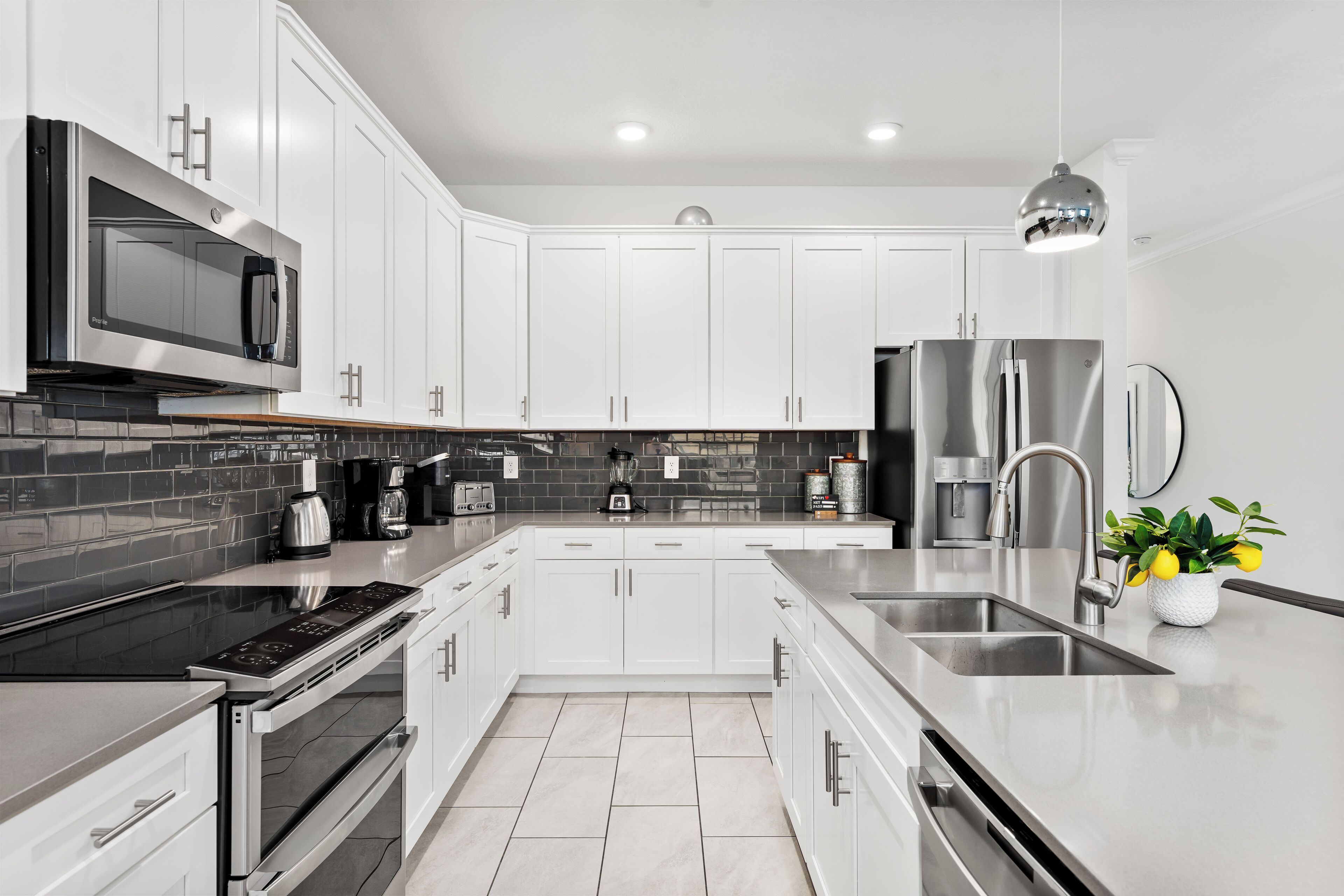 A modern kitchen with white cabinets, stainless steel appliances, a black countertop, and a backsplash.