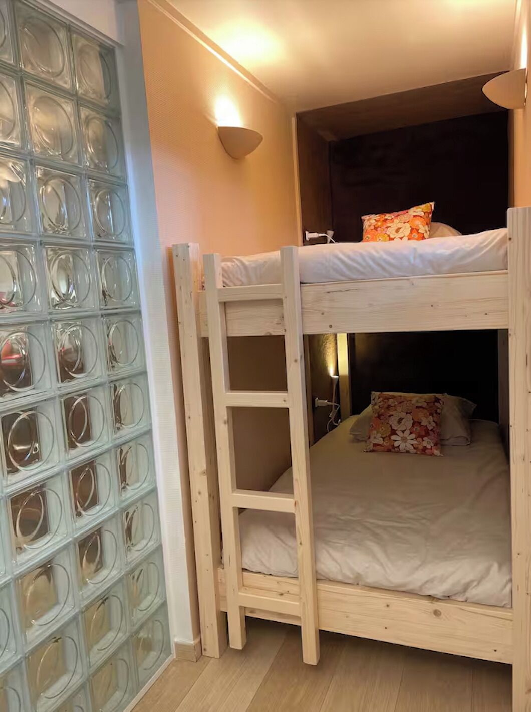 A bunk bed with a ladder, a wall with circular glass panels, and a wall-mounted light fixture.