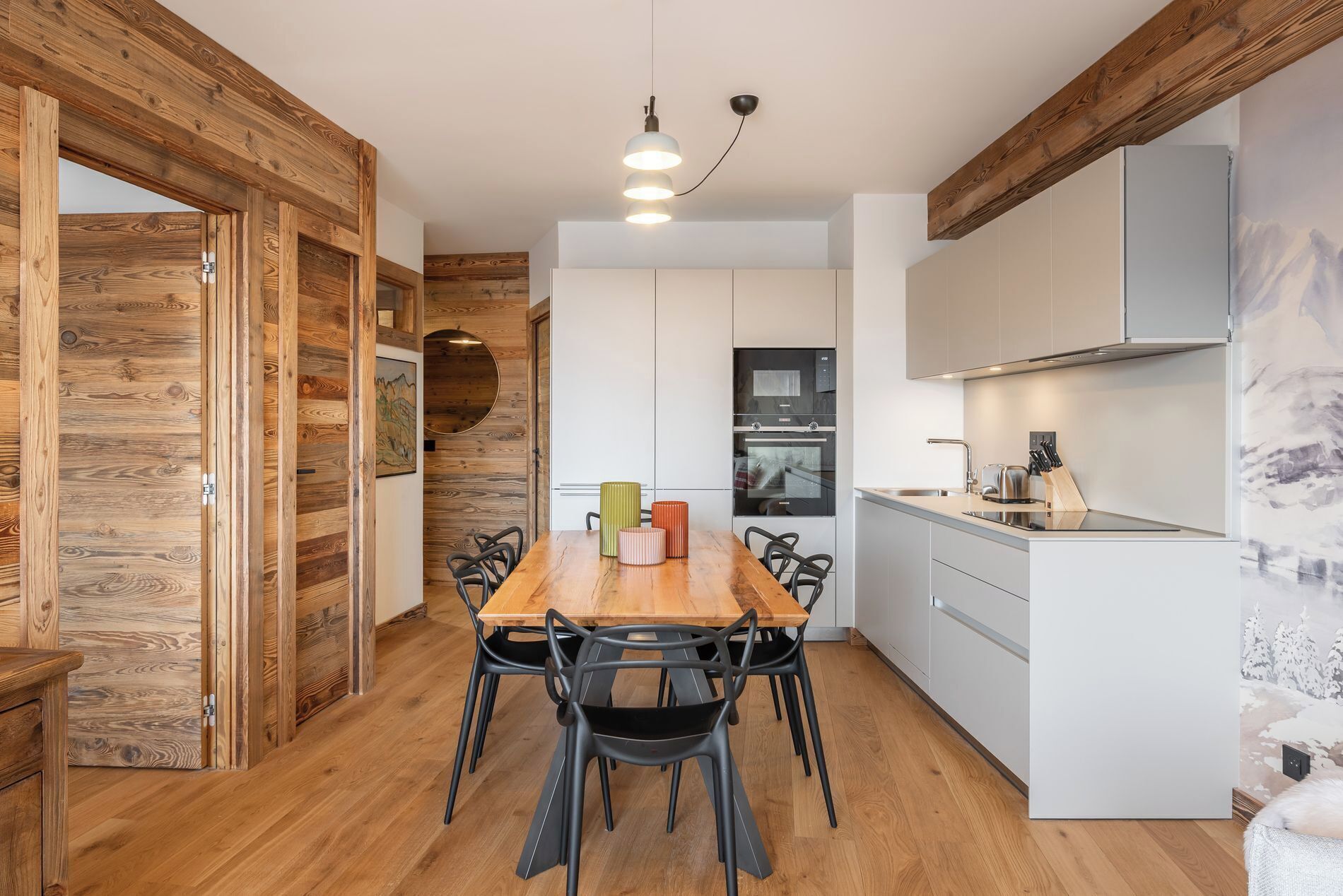 A modern kitchen with white cabinets, a wooden dining table with chairs, and a hanging light fixture.