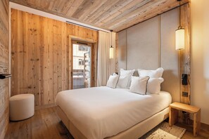 A bedroom with a wooden ceiling, a large bed with white bedding, a bedside table, and a wall-mounted lamp.