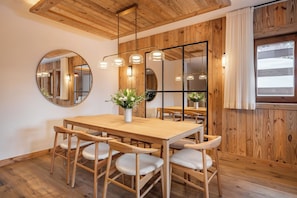 A dining area with a wooden table and chairs, a round mirror, and pendant lights.
