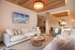 A modern living room with a large sofa, two round wooden tables, and a dining area with a wooden table and chairs.