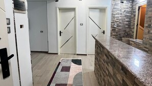 A hallway with two doors, a patterned rug, a kitchen area with a granite countertop, and a stone backsplash.