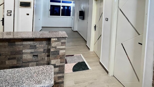 A hallway with a granite countertop, a patterned rug, and a view of a room with a window.