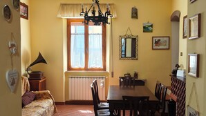 Un coin repas avec un sol en briques, une table entourée de chaises, un lustre et une fenêtre agrémentée de rideaux.