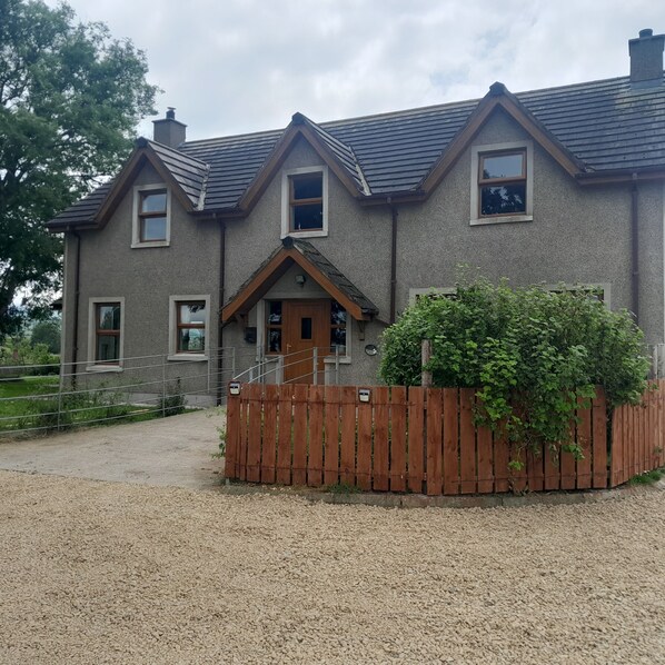 Une maison à deux étages avec une allée en gravier, une clôture en bois et un petit jardin.