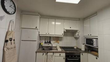 Una pequeña cocina con armarios blancos, un refrigerador, un microondas y un lavamanos.