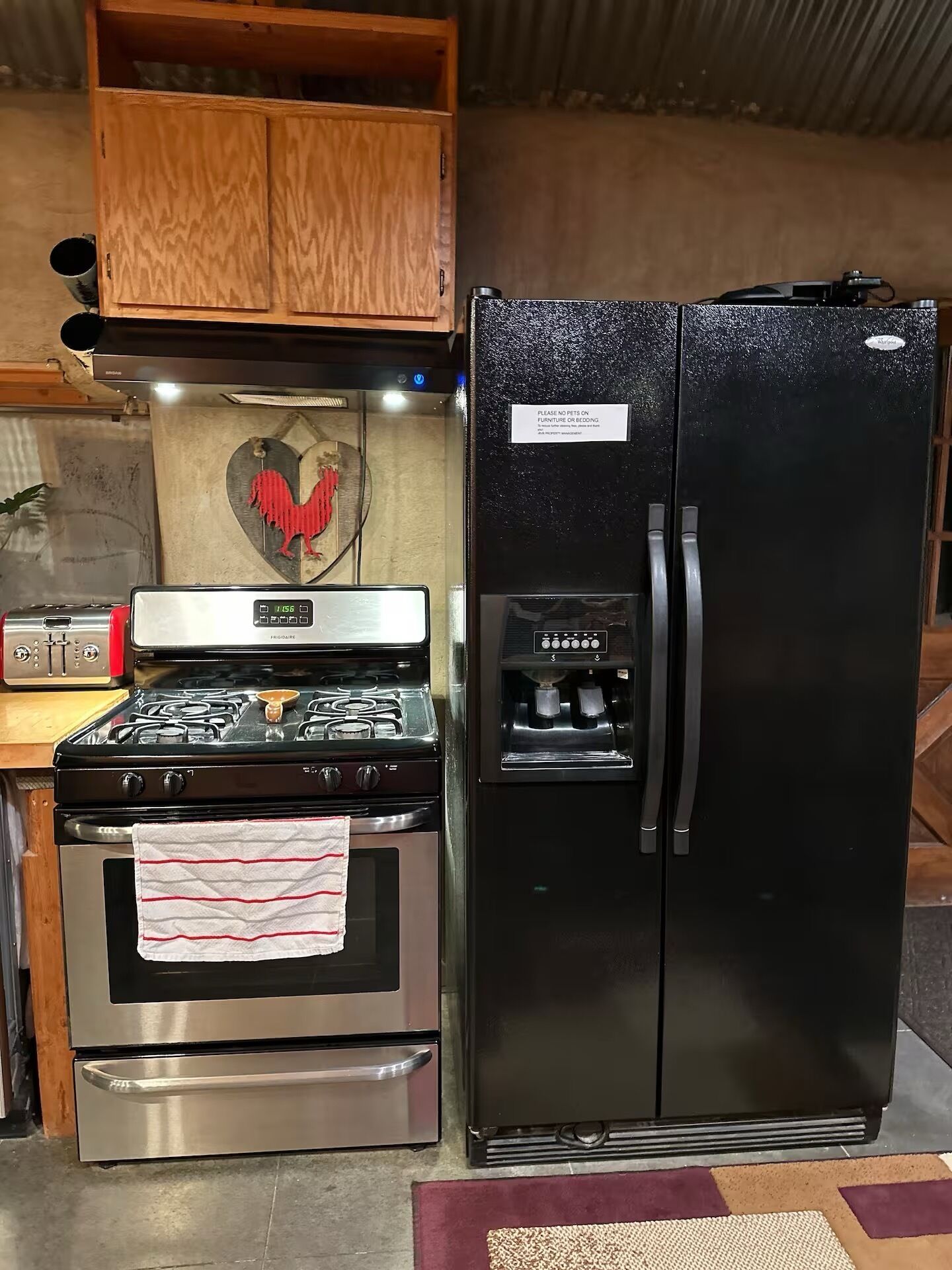 A kitchen with a stainless steel stove, a black refrigerator, and wooden cabinets.
