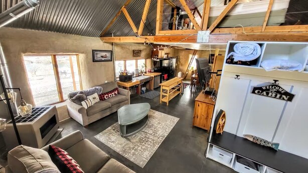 A spacious loft with a high ceiling, a kitchen area, a living room with a sofa and a coffee table, and a 'Welcome to Cabin' sign.