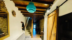 Un couloir avec un canapé gris, un plafond en bois, un mur en pierre et une porte en bois.