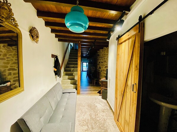 A hallway with a grey sofa, a wooden ceiling, a stone wall, and a wooden door. - Anibal Village House (Fermoselle)