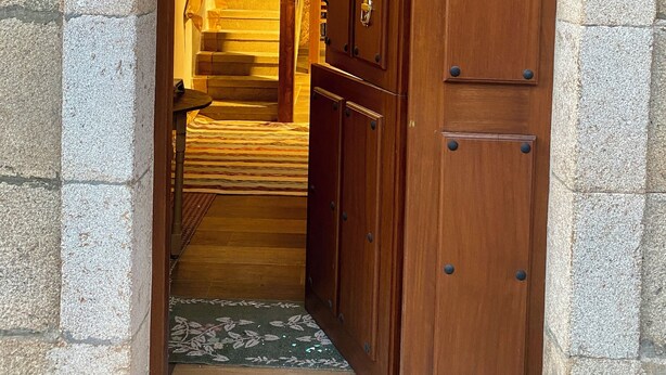 Un portail en pierre en arc de cercle mène à un escalier en bois, au-dessus duquel se trouve un luminaire vert.