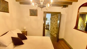 Une chambre avec un grand lit, un lustre, un mur en pierre et un plafond en bois.