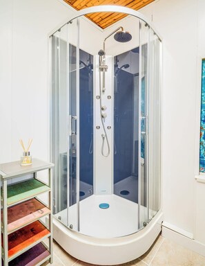 Een moderne douchecabine met glazen deur, houten plafond en een klein tafeltje met kandelaar.