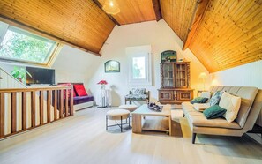 Een knus loft-achtig woongedeelte met een houten plafond, een bank, een salontafel en een televisie.