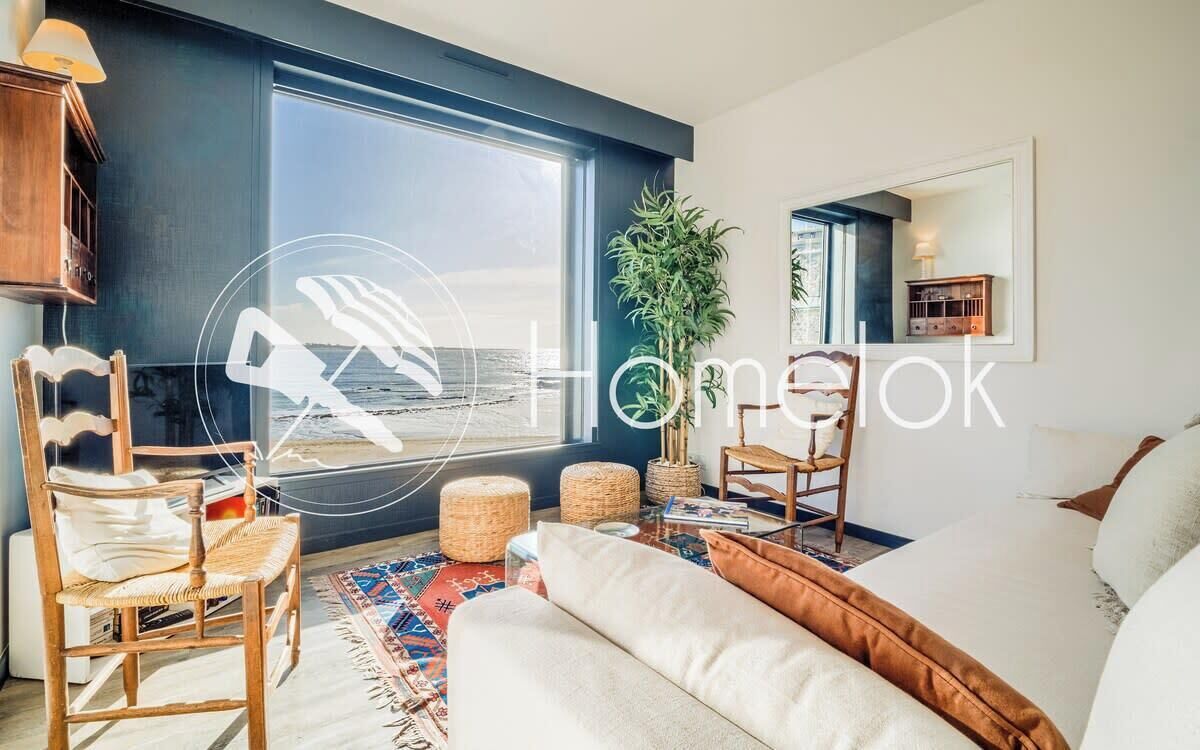 Ein modernes Wohnzimmer mit großem Fenster, einer Couch, einem Sessel und einem kleinen Tisch.