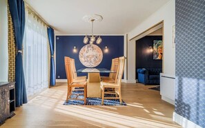 A dining area with a round table and chairs, a chandelier, and a wall with a large circular artwork. - Charme et standing à deux pas de la mer (Ploemeur)