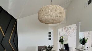Een eethoek met een donker houten tafel, gedekt voor vier personen, witte borden en wijnglazen. Daarboven hangt een geweven lamp.