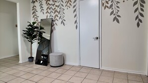 Een gang met een witte deur, een potplant, een spiegel en een muur met bladmotieven.
