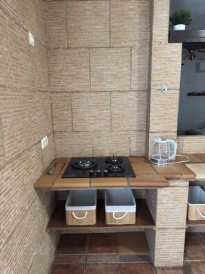 Una cocina compacta con protector contra salpicaduras de ladrillo, una estufa a gas y dos contenedores de almacenamiento.