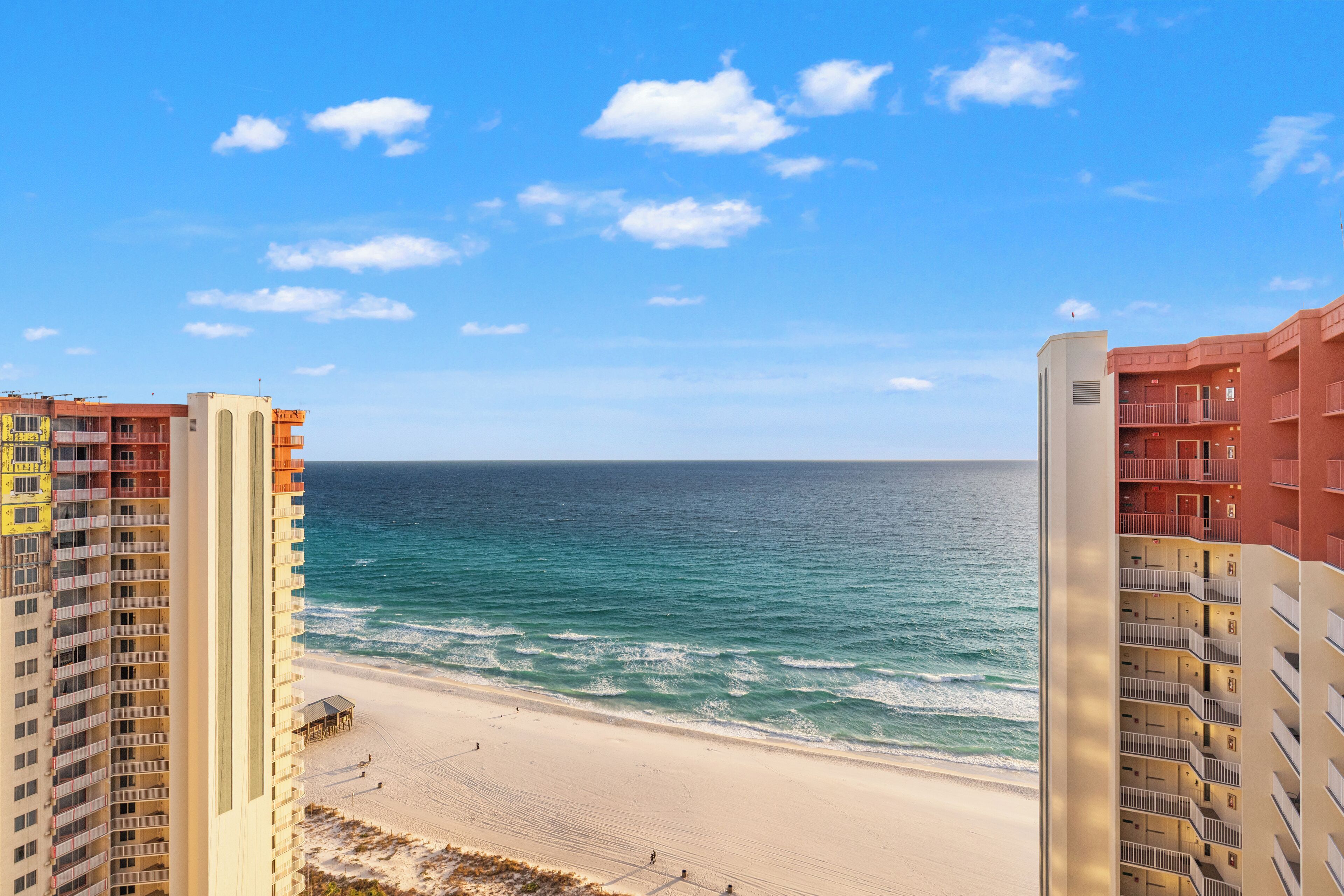 Een hotel aan het strand met meerdere verdiepingen, een zandstrand en de oceaan op de achtergrond.