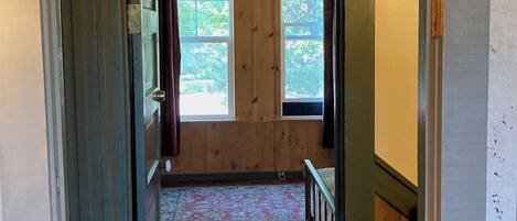 A narrow hallway with wooden flooring and a window at the end.